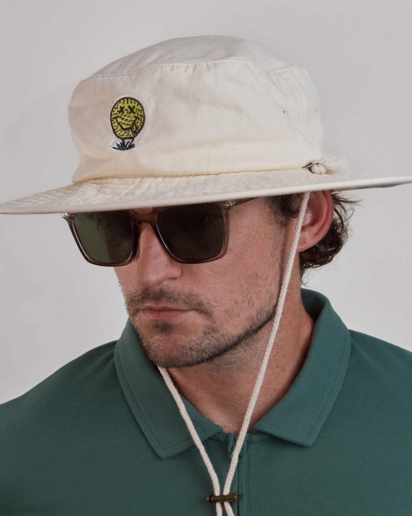 A man wearing an off-white cotton canvas boonie hat featuring a yellow smiley golf ball design.
