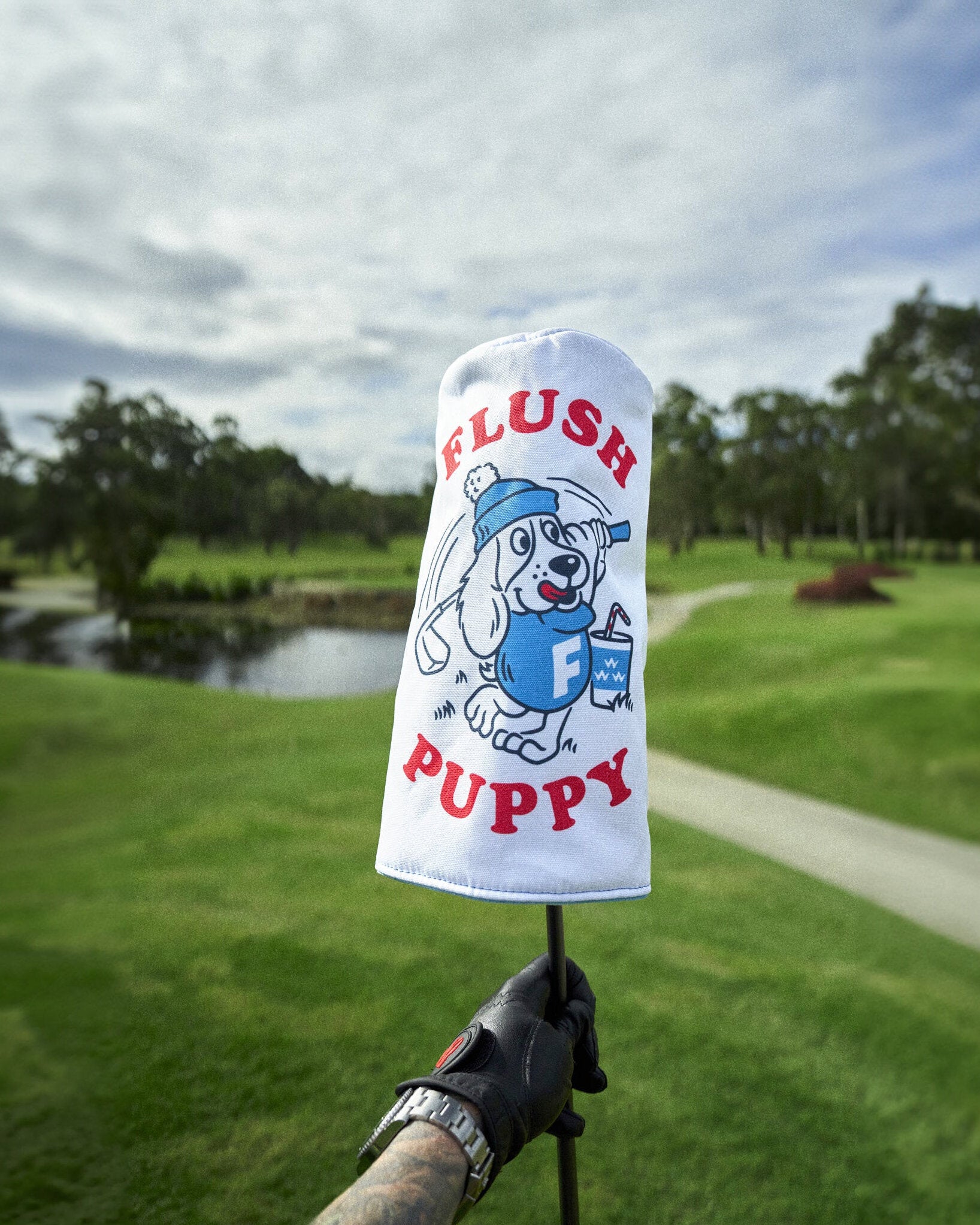 A white headcover featuring a cartoon puppy graphic in blue and red, held upright on a golf course.