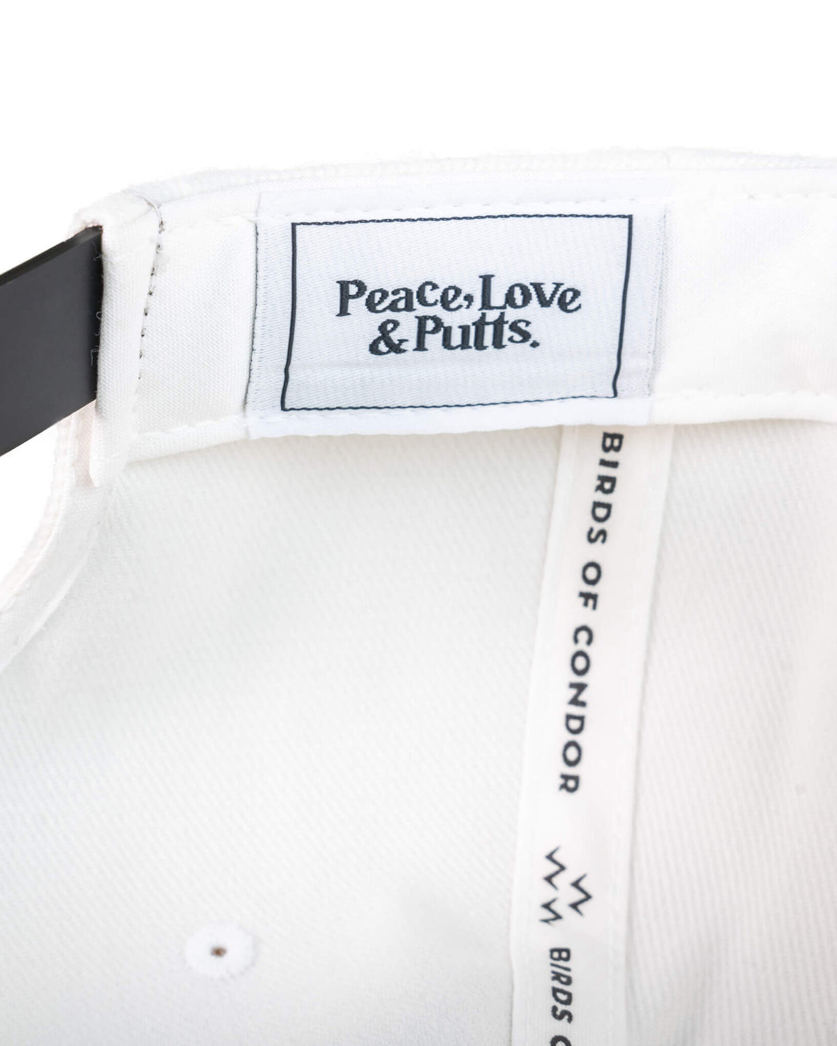 Detail of a white snapback's interior, showing a woven label reading Peace, Love & Putts.