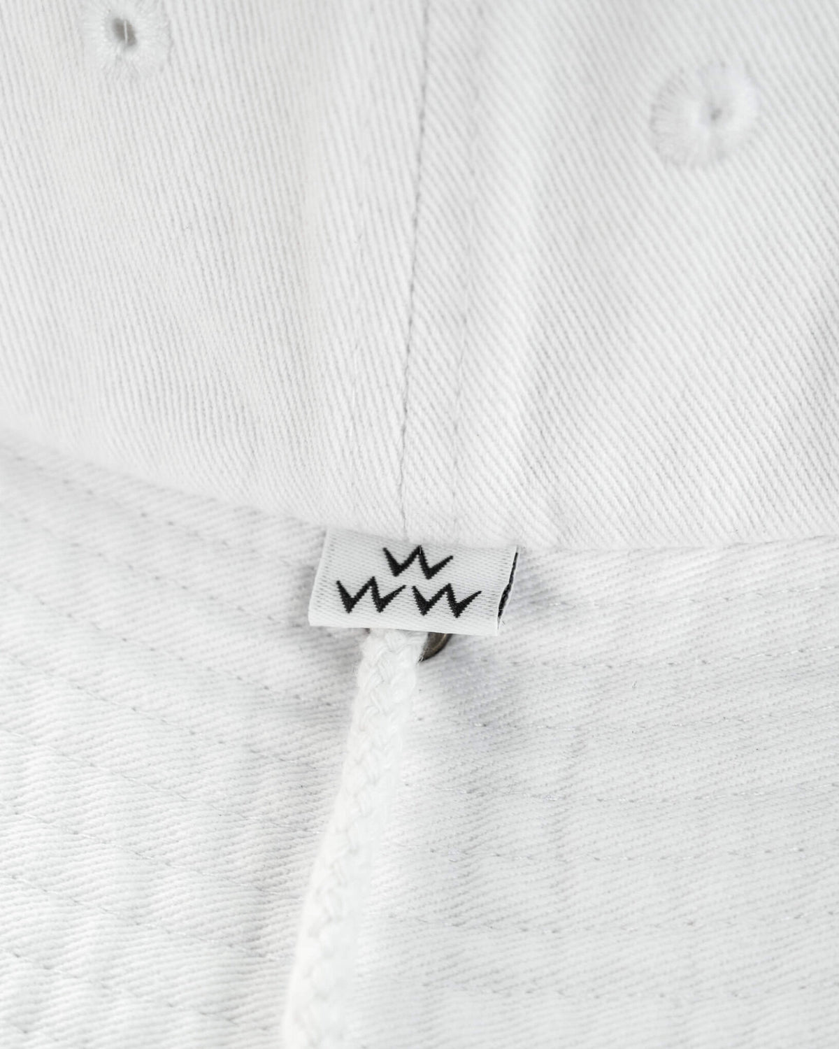 Detail of a white boonie hat featuring a small black crown logo label above the chin strap.