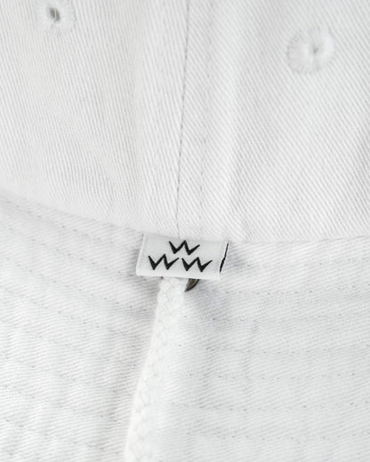 Detail of a white boonie hat featuring a small black crown logo label above the chin strap.