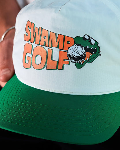 Detail of a white snapback cap with a green brim and an orange and green alligator graphic.