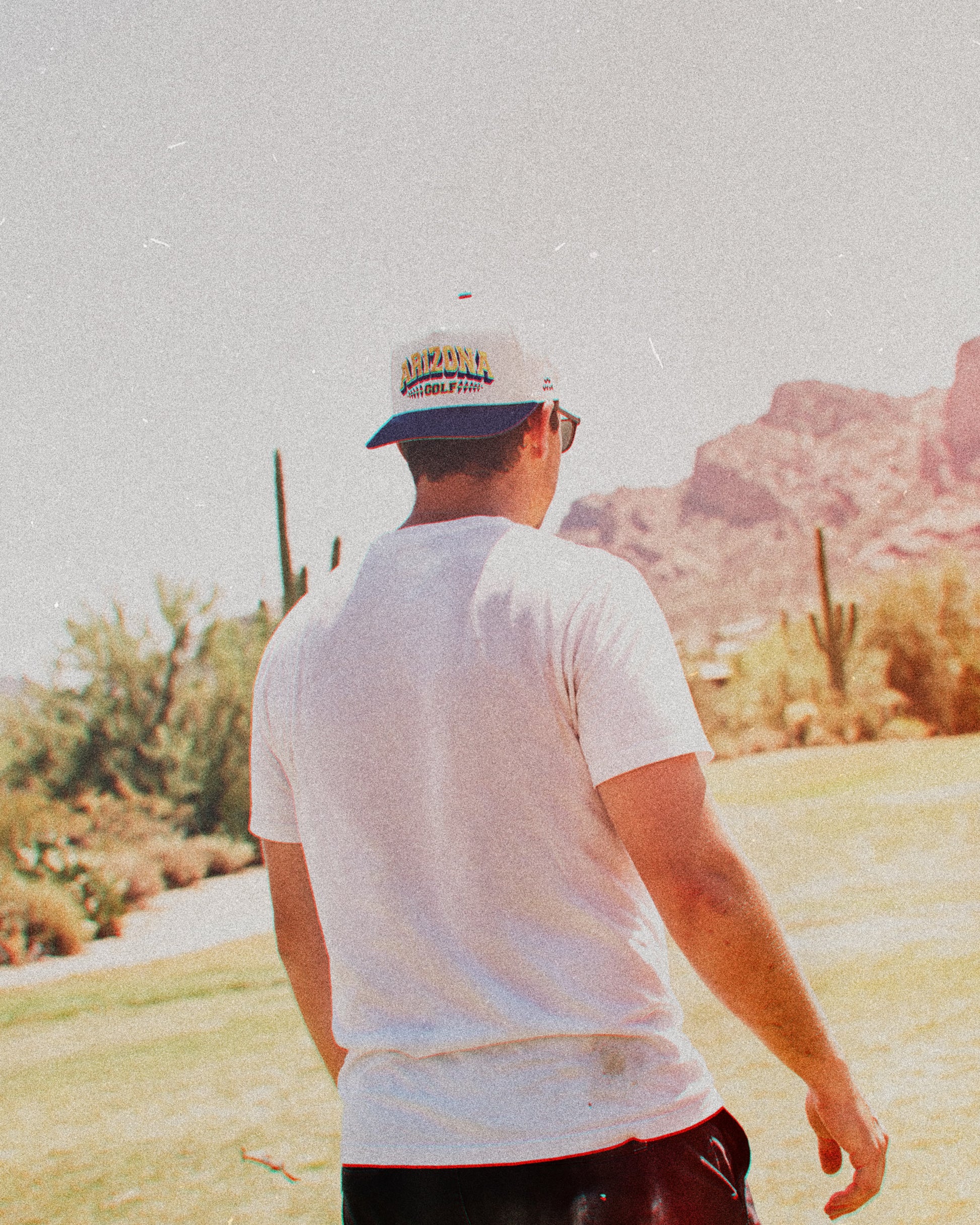 A man wearing a white snapback with a navy brim and embroidered Arizona Golf text on the front.