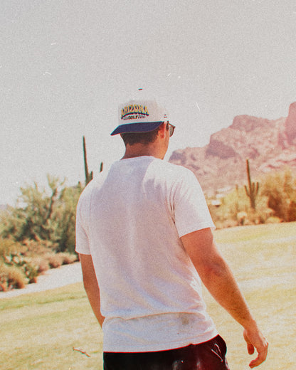 A man wearing a white snapback with a navy brim and embroidered Arizona Golf text on the front.