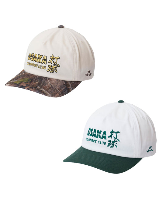 Two baseball caps shown on a plain white background: one in off-white with a camouflage brim and gold embroidered text reading Osaka Country Club, and one in white with a dark green brim and green embroidered text reading Osaka Country Club.