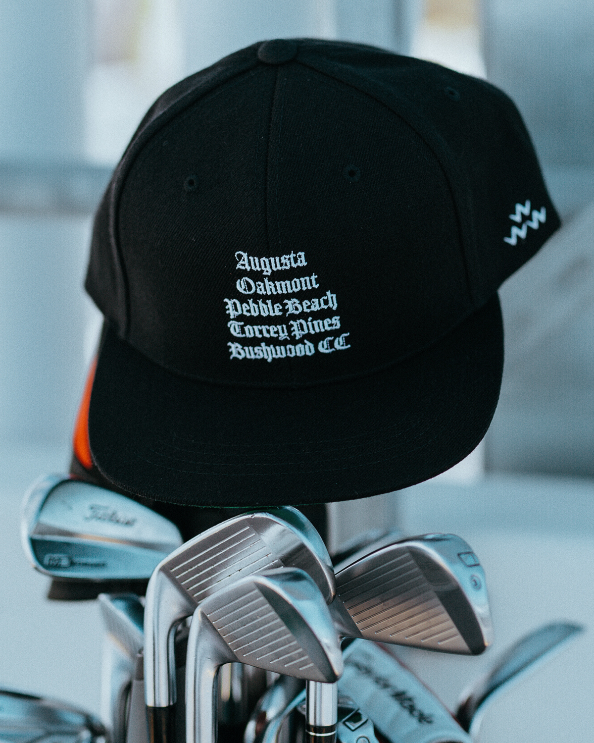 Front of a black snapback cap featuring white text on the crown and a small logo on the side panel.