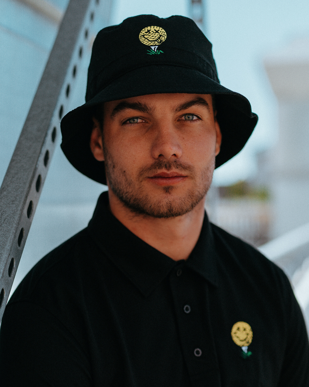 A man wearing a black bucket hat with a yellow and green embroidered golf ball tee design on the front.