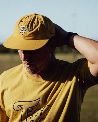 A person wearing a mustard strapback cap and a matching t-shirt with embroidered Tiger logos.