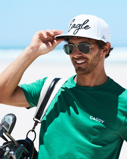 White snapback cap with black cursive Eagle script across the front, worn outdoors with sunglasses.
